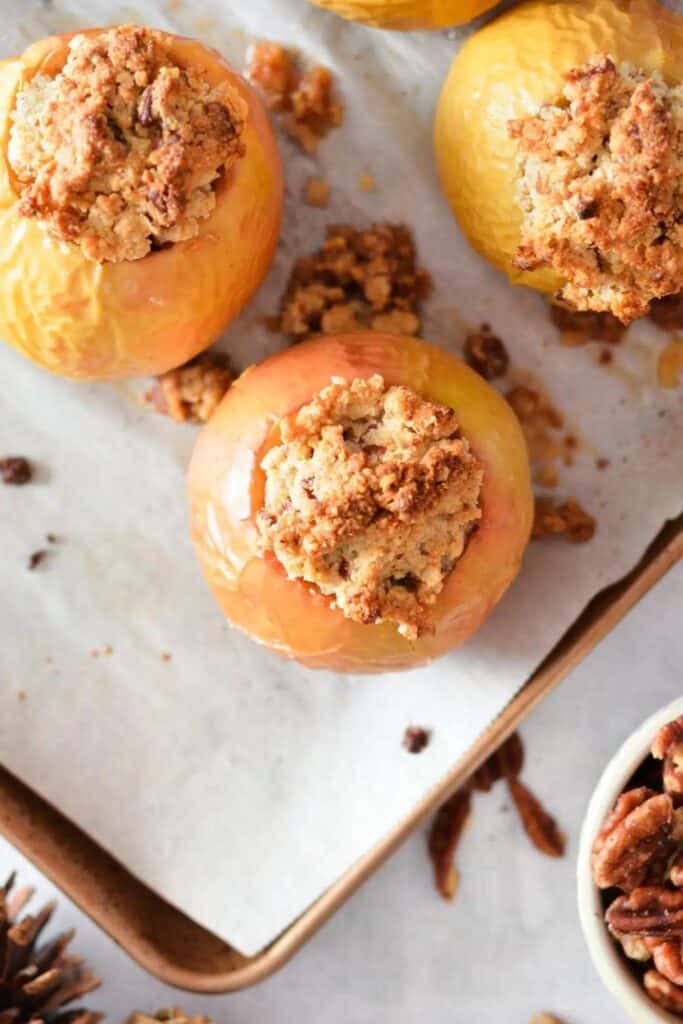 Three baked apples with crumble topping on a baking sheet.