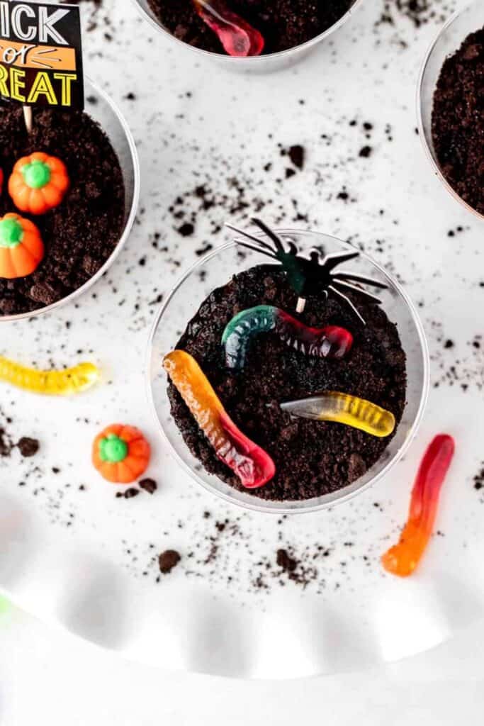 Plastic cups of healthy halloween dirt cups made with pudding, oreo crumbs and topped with gummy worms.