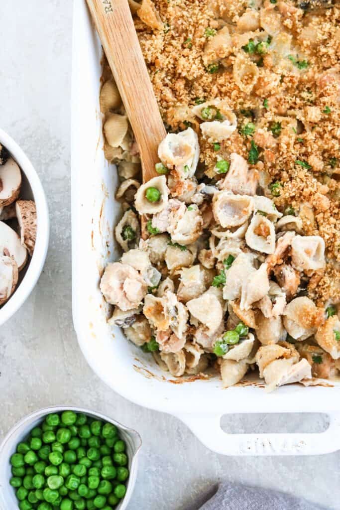 Healthy tuna noodle casserole with pasta shells, chunks of tuna, green peas and mushrooms in a creamy sauce, topped with golden breadcrumbs and fresh parsley.