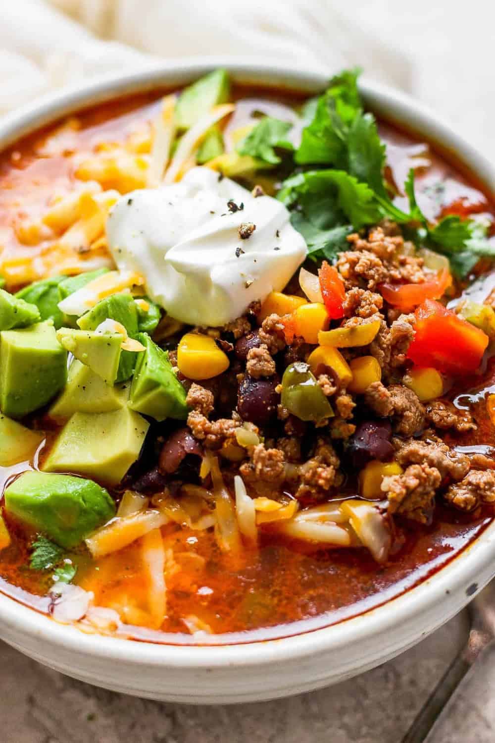Hearty homemade taco soup with seasoned ground beef black beans corn and tomatoes in a rich tomato broth. The soup is topped with avocado shredded cheese sour cream and fresh cilantro.