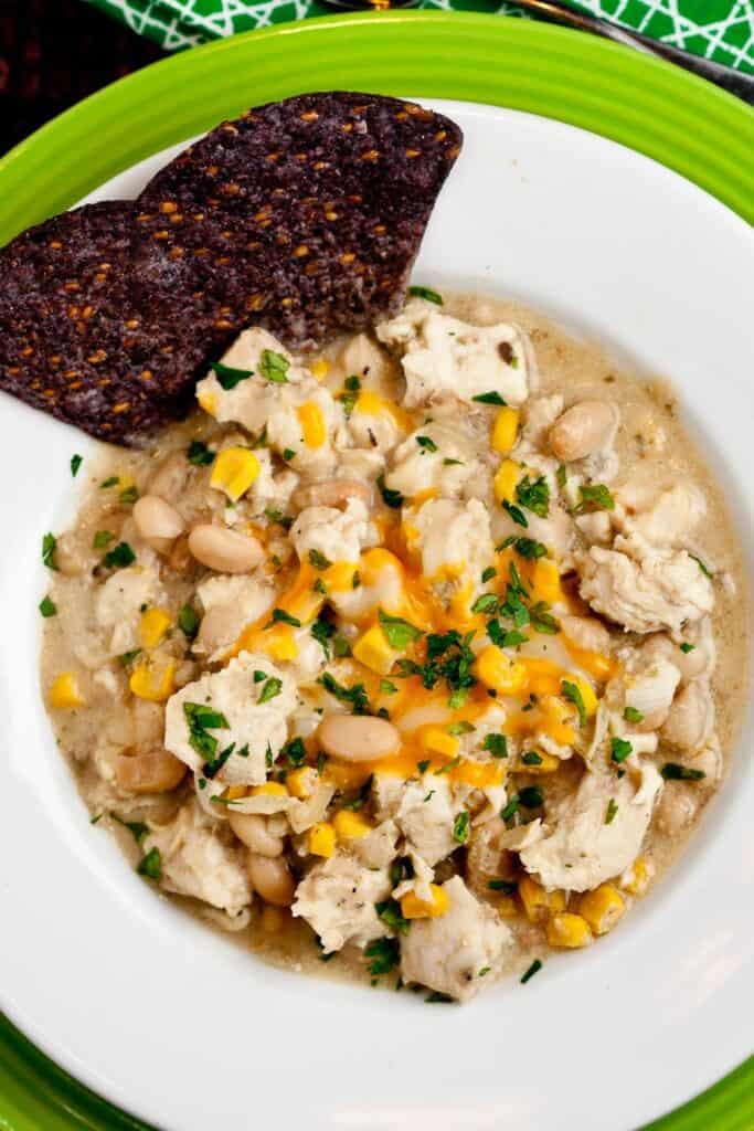 Close up of a ceramic soup bowl filled with white bean chicken chili, with corn and sprinkled with cilantro. 