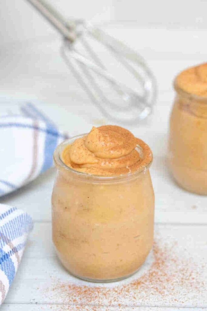 Creamy pumpkin pudding served in a small glass jar with a soft swirl on top and a dusting of cinnamon. The individual portions can be chilled in advance for easy fall desserts make ahead.