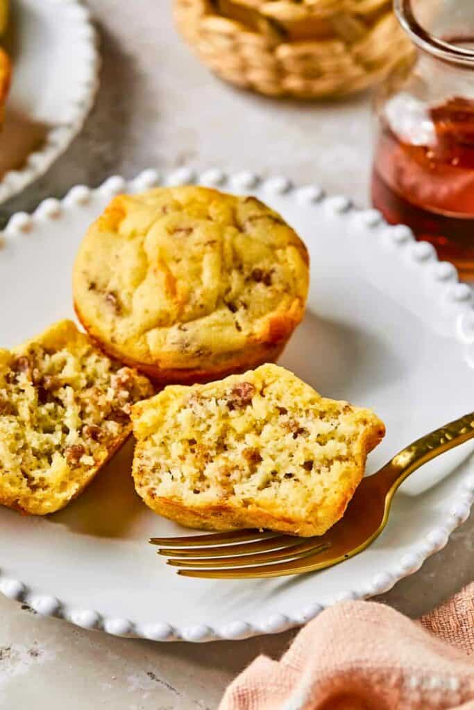 Sweet and savory McGriddle muffins with a soft golden exterior and a fluffy interior filled with sausage crumbles. One muffin is split open on a plate to show the tender crumb while a fork and maple syrup sit nearby.