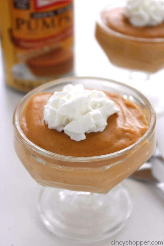 Glass pudding cup filled with homemade pumpkin pudding topped with whipped cream.