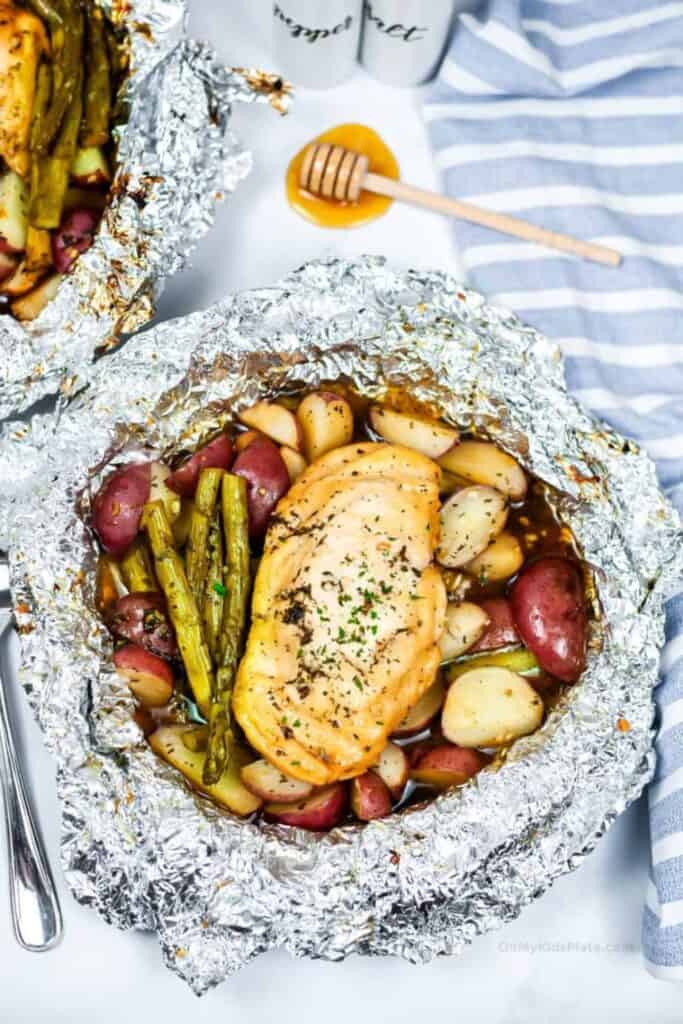 A round foil pouch filles with honey garlic marinated chicken breast with asparagus and baby red potato halves. 