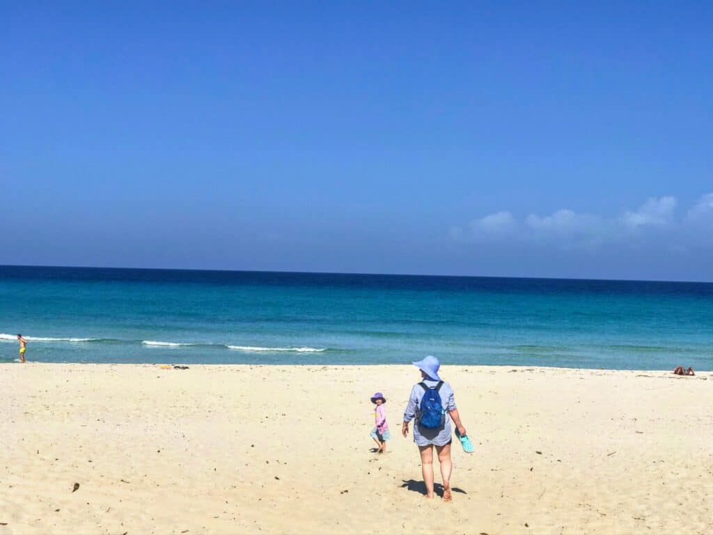 Mom and daughter walking barefoot in the sand, towards the ocean in Varadero, Cuba