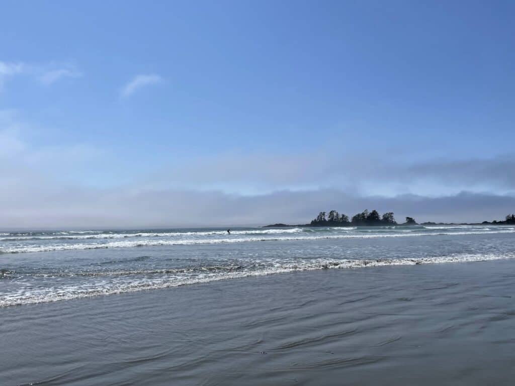 Waves crashing into the shore of sandy beach with surfers and two small islands on Chesterman Beach Tofino.