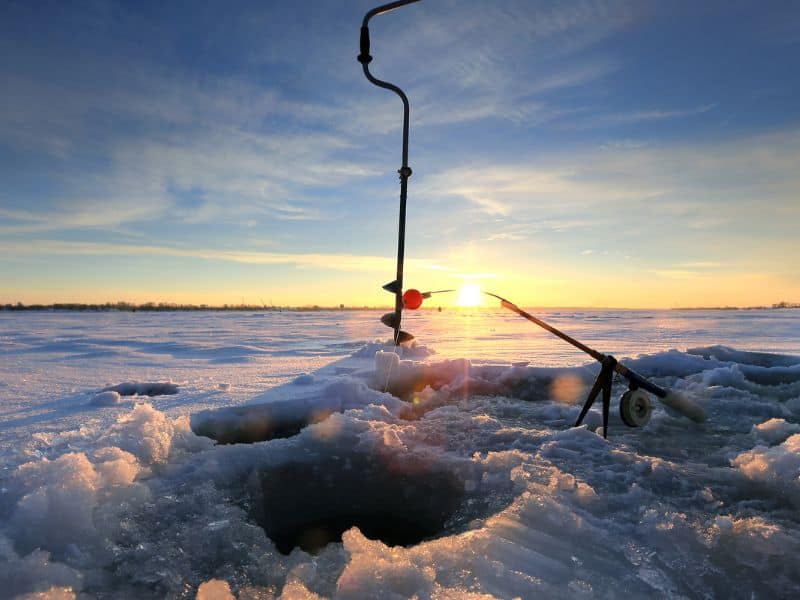 Ice fishing hole, drill and rod on frozen lakae at sunrise. 