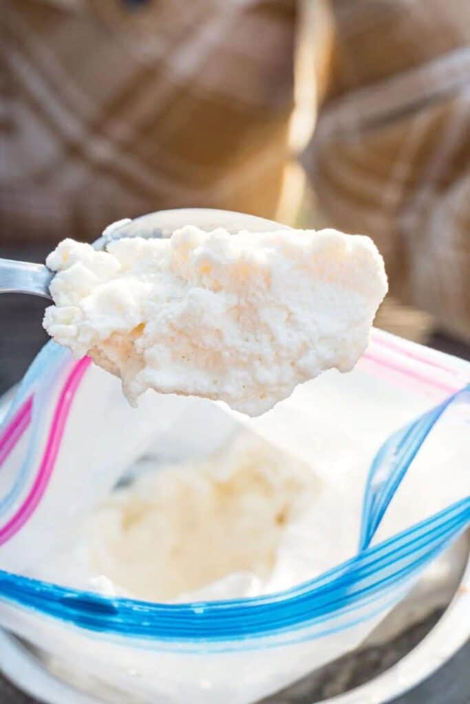 Spoon holding ice cream over a ziploc bag of homemade ice cream.