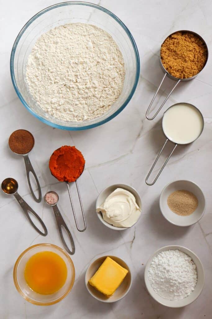 Ingredients for pumpkin cinnamon rolls laid out in bowls, measuring cups and teaspoons.