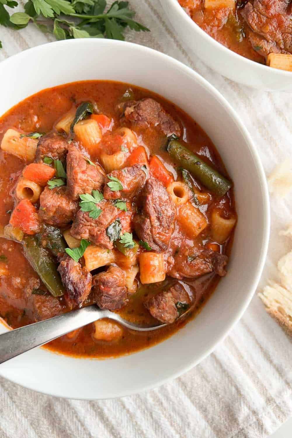 Italian beef soup with tender chunks of beef pasta green beans and vegetables in a rich tomato broth. Fresh parsley tops the hearty soup for a quick dinner.