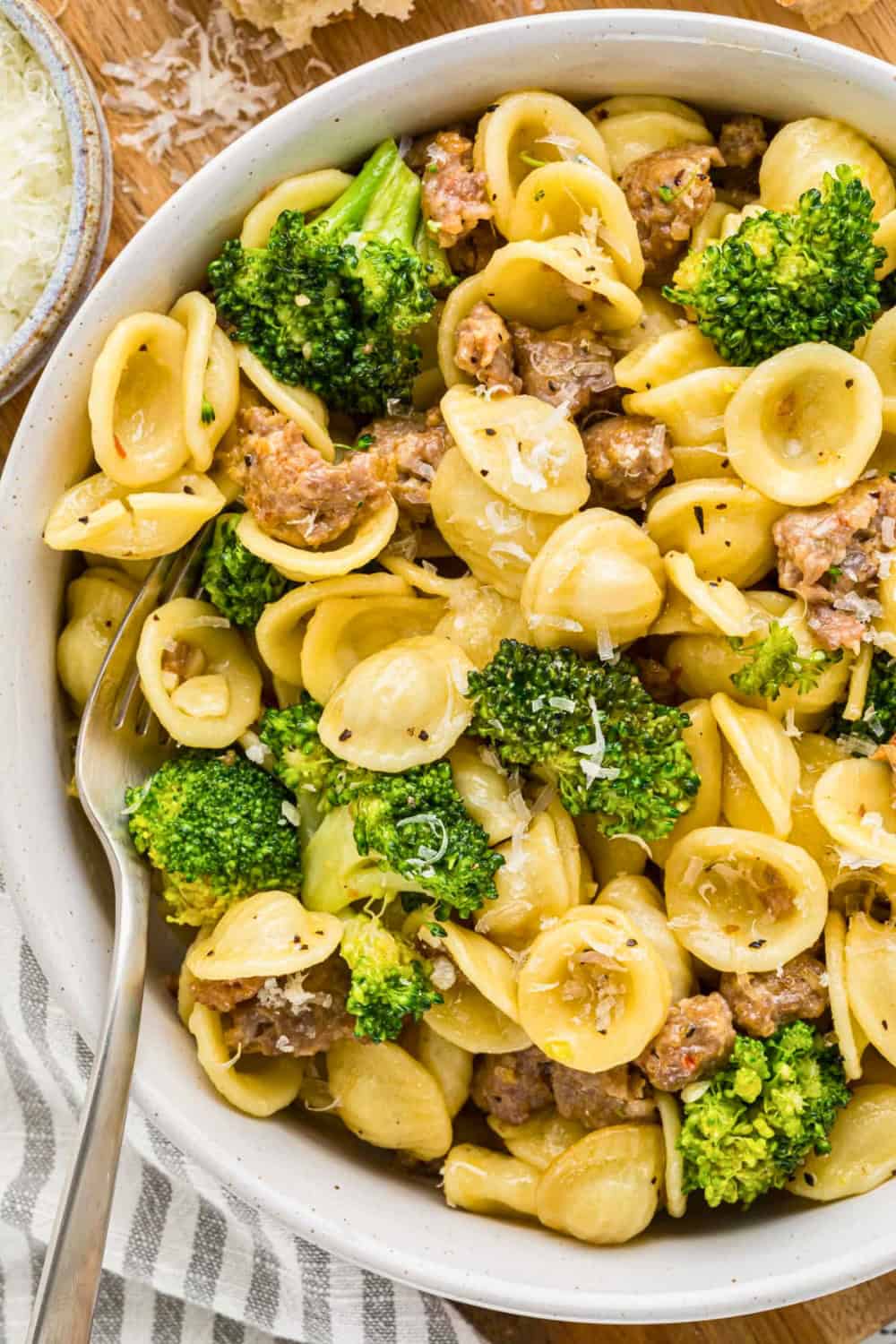 Italian sausage and broccoli pasta made with orecchiette, browned sausage, and tender broccoli florets tossed together in a large serving bowl. A light sprinkling of grated Parmesan cheese finishes the dish.