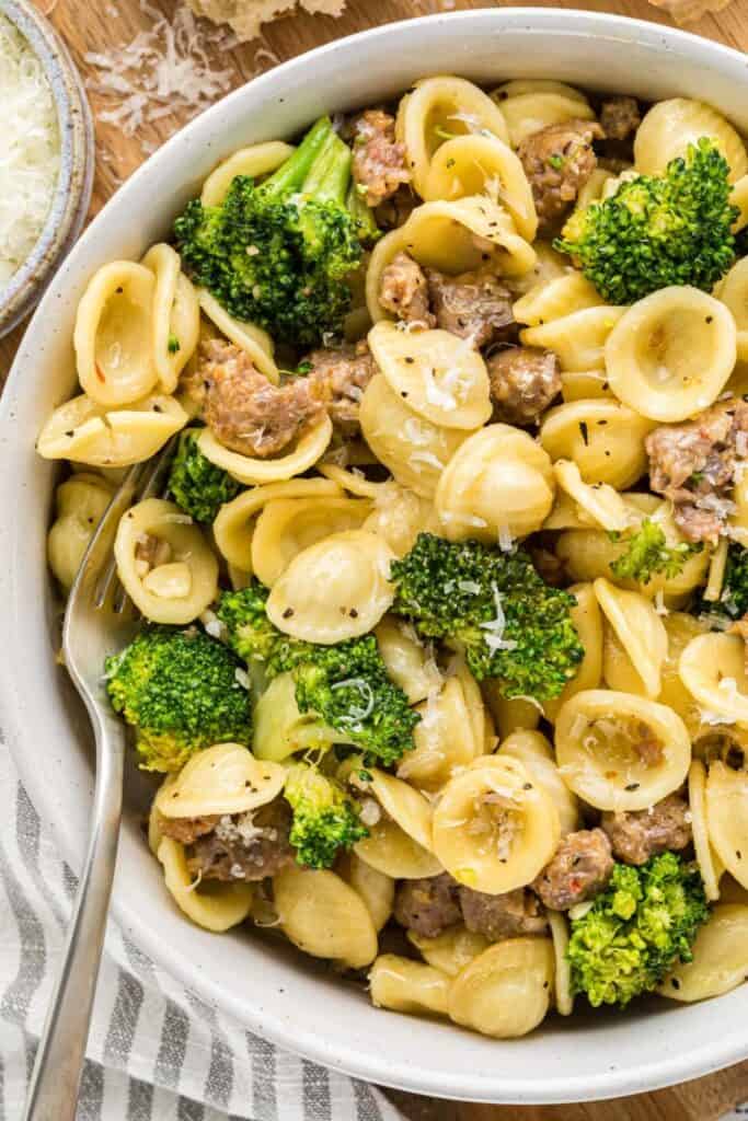 Italian sausage and broccoli pasta with small shell pasta tossed with browned sausage, tender broccoli florets, and grated parmesan. The pasta is served in a large bowl with a fork and sprinkled with cheese for a quick and easy family dinner.