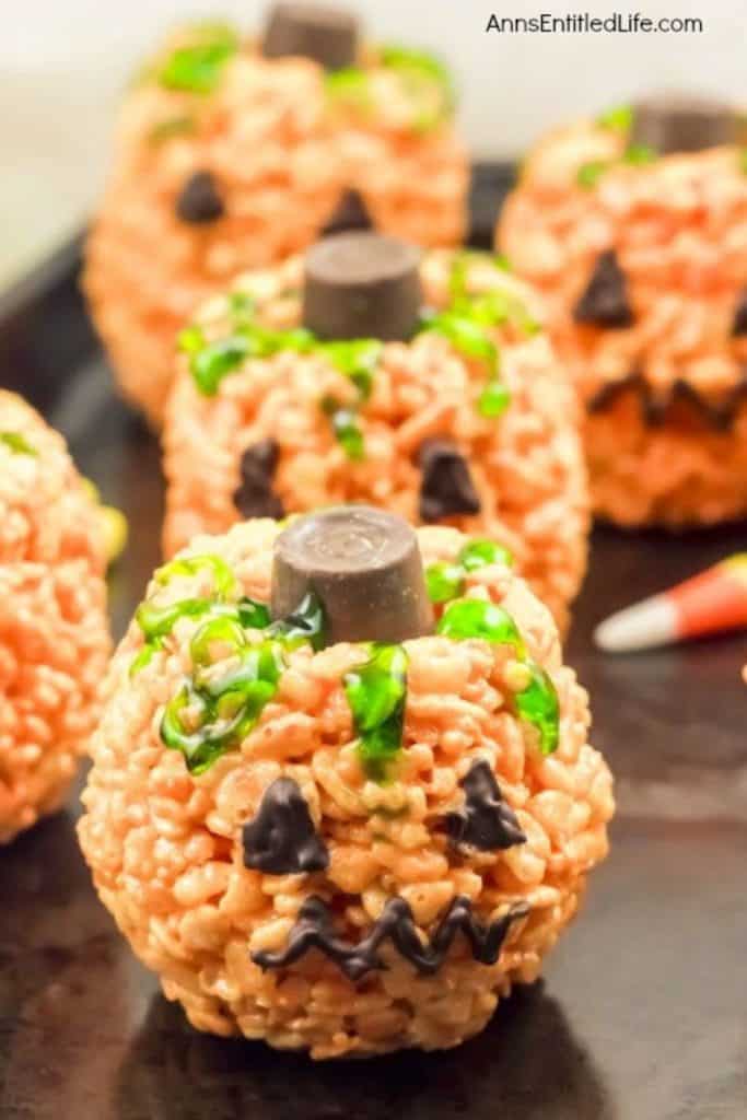 Jack O’ Lantern Halloween treats made from orange Rice Krispies shaped into pumpkins, decorated with chocolate icing faces, green icing vines, and topped with a chocolate candy stem.