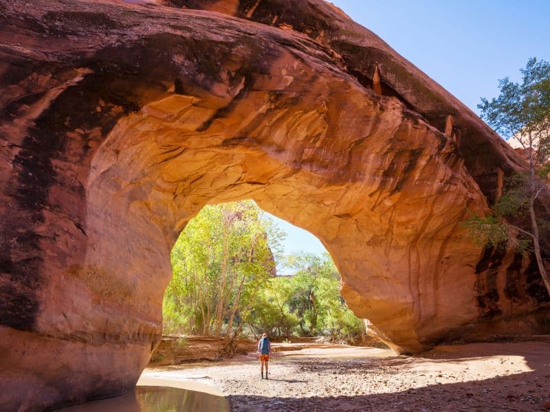 Man hiking under the Jacob Hamblin Arch in the Grand Staircase - Escalante National Monument