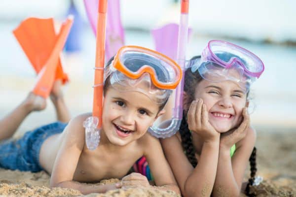 Young boy and girl lying on bellies on sandy Hawaiian beach, wearing snorkel gear.