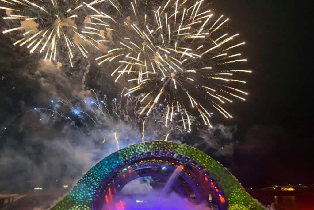 A burst of golden fireworks lights up the night sky above the colorful, arch-shaped stage of the Kiss of the Sea show on Phu Quoc Island, with smoke and lights creating a festive atmosphere.