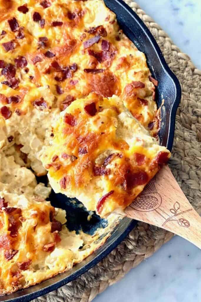 Cast iron pan with loaded hashbrown casserole cheddar cheese and crumbled bacon.