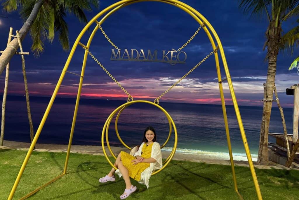 Young girl wearing a dress, seated on a swing seat with a beach sunset in the background on Long Beach, Phu Quoc Island Vietnam. 