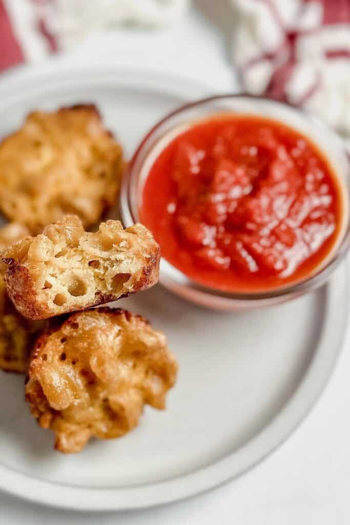 Close up of Mac and Cheese bites beside a bowl of tomato dipping sauce. 