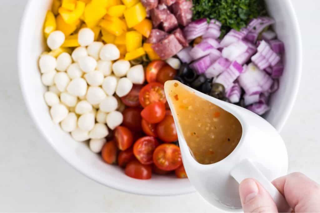 Italian dressing being poured into a bowl of pasta salad ingredients. 