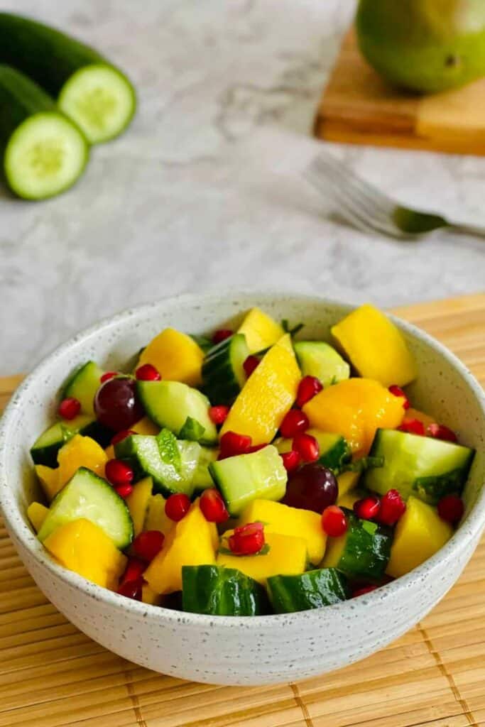 Bowl of mango, cucumber salad with pomegranate seeds sprinkled on top. 