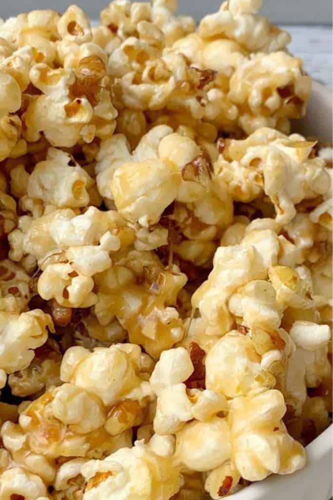 Close up of a bowl filled with sticky caramel popcorn, freshly made and ready to be shared during a family movie night. The popcorn glistens with melted caramel, highlighting its sweet, crunchy texture.