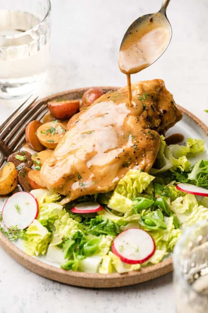 Plate with green salad, and  a maple dijon chicken breast with sauce being poured over it from a spoon.