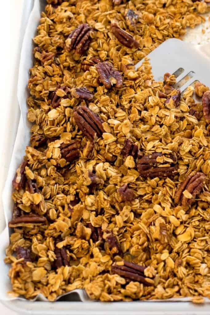 Tray of maple pecan granola, with a spatula dipping into the granola.