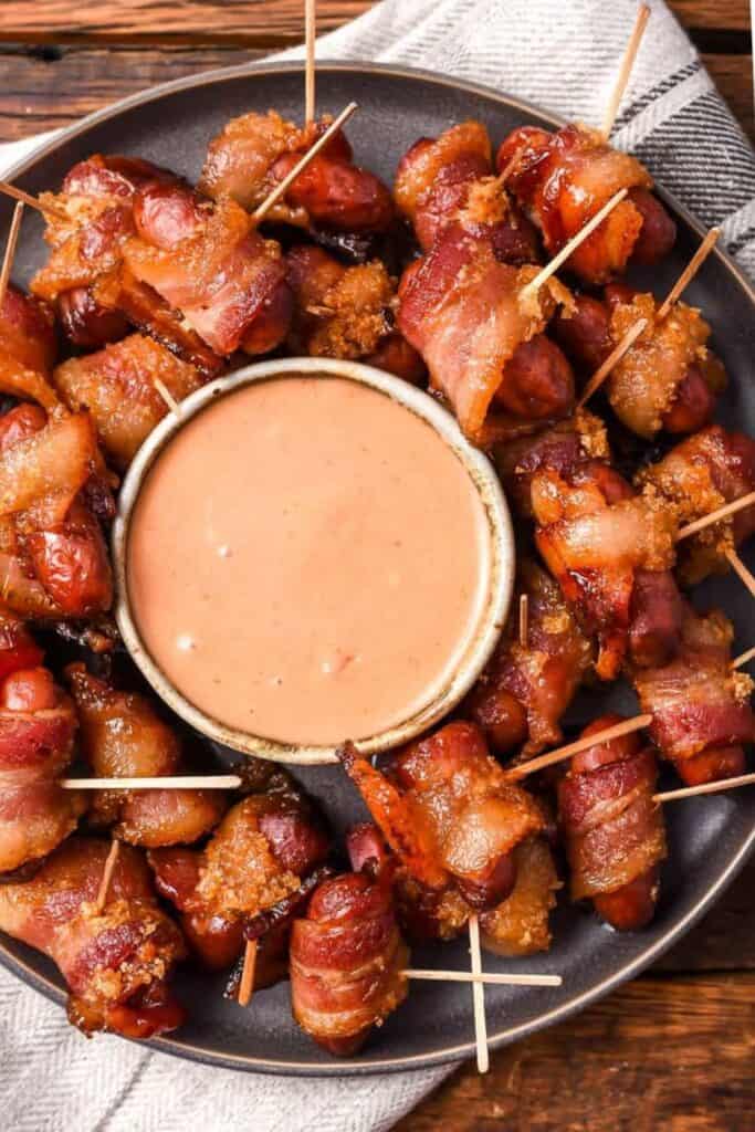 Mini smokies wrapped in sweet bacon with a bowl of spicy dipping sauce.