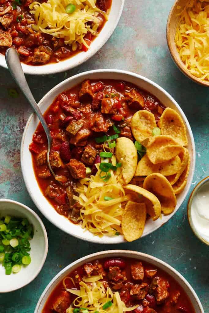 Bowl of stek chili topped with cheddar cheese and corn chips. 