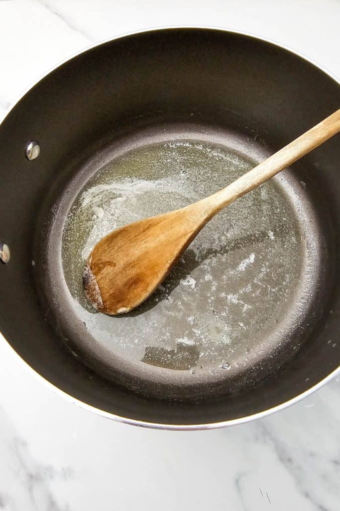 Melted butter in a nonstick saucepan being stirred with a wooden spoon, the first step in making zombie brains rice krispie treats.