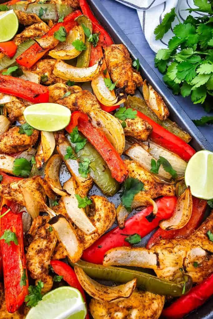 Mexican fajita recipe baked on a sheet pan with seasoned chicken strips, roasted red and green bell peppers, and tender onion slices. Garnished with fresh cilantro and lime wedge.
