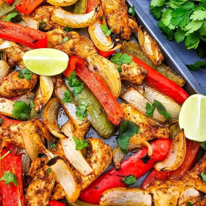 Mexican fajita recipe baked on a sheet pan with seasoned chicken strips, roasted red and green bell peppers, and tender onion slices. Garnished with fresh cilantro and lime wedge.