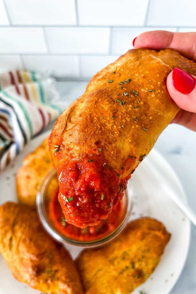 Close up of a hand holding a Mini Pepperoni Calzone dipped in tomato sauce. 