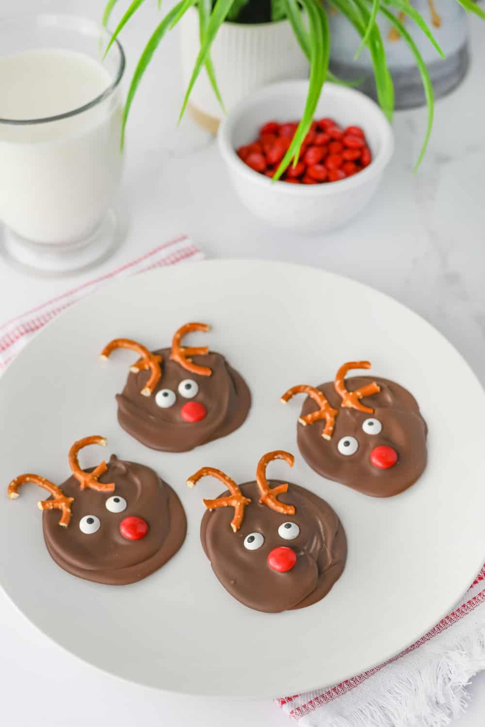 Four mini chocolate reindeer Christmas treats with pretzel antlers, candy eyes, and bright red candy noses arranged on a white plate.