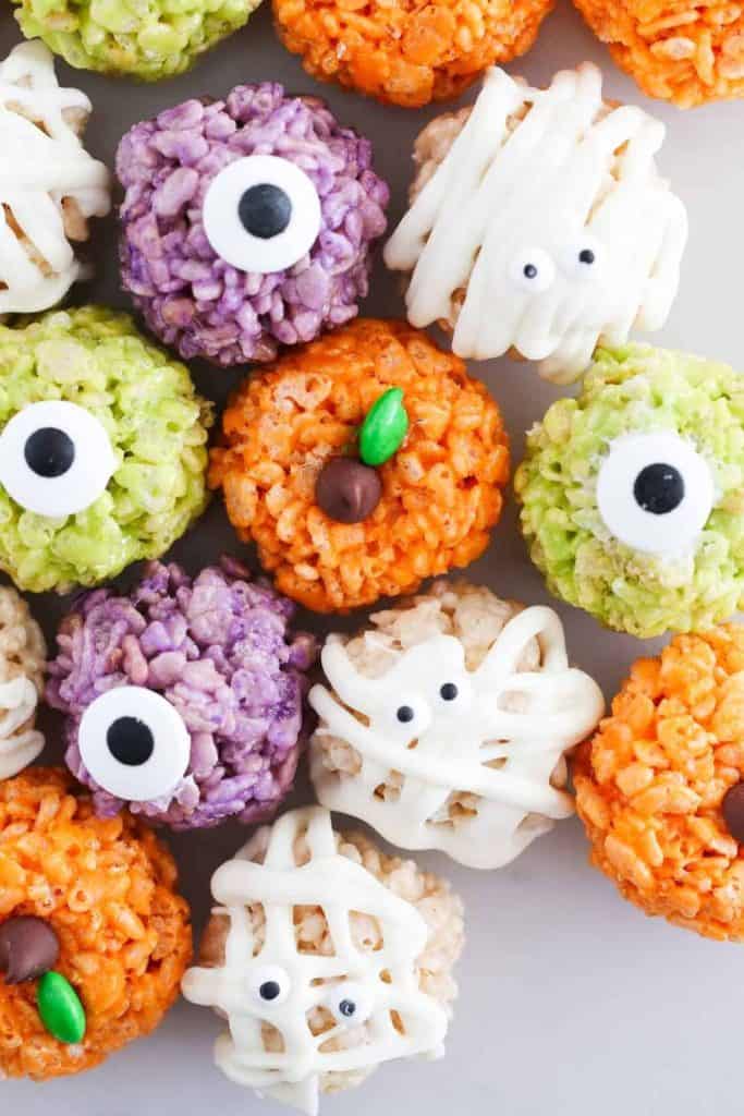 Colorful Halloween Rice Krispies treats shaped into mummies, monsters, and pumpkins, decorated with candy eyes, white icing bandages, and chocolate candy stems.