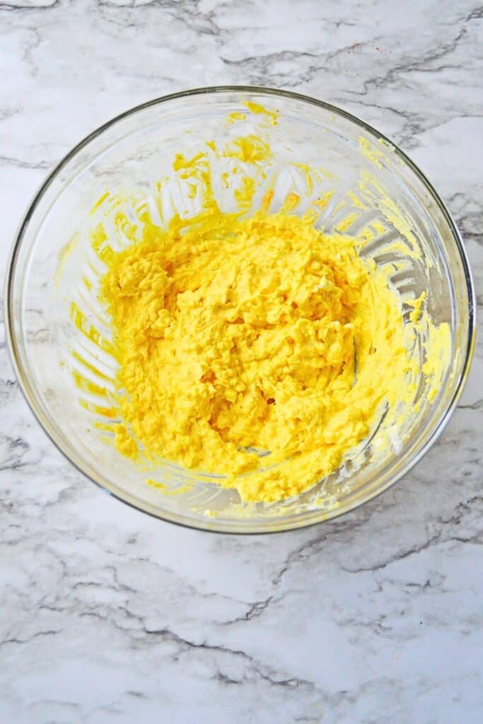 Overhead view of a creamy yellow deviled egg filling mixed with egg yolks, mayonnaise, mustard, and seasonings in a clear glass bowl.