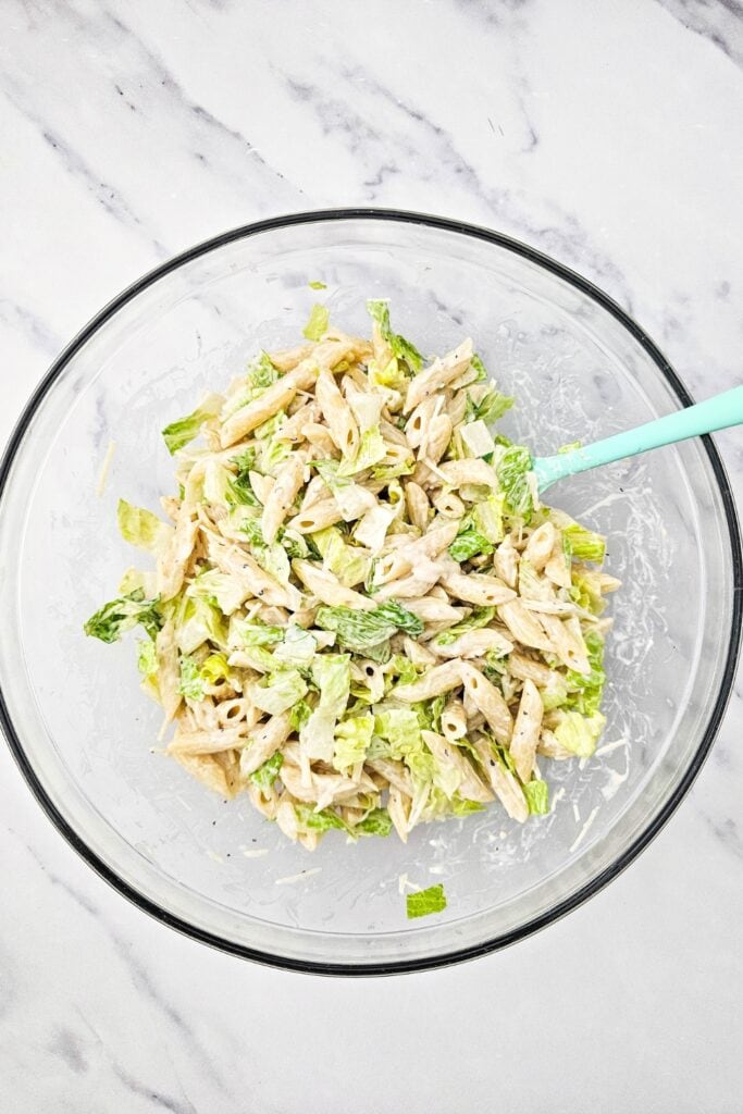 Creamy Caesar pasta salad with penne and chopped romaine tossed together in a glass bowl with dressing, shown as a quick side dishes option that is easy to mix and serve.