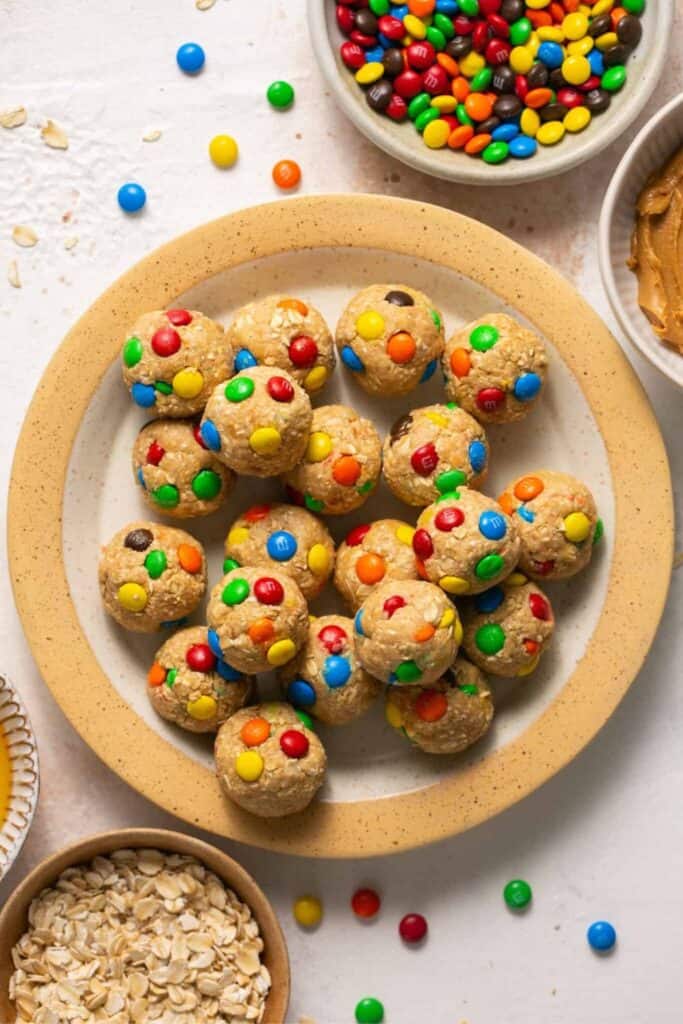 Plate filled with Monster Cookie Protein Balls and tiny bowls of peanut butter, M&Ms and oats. 