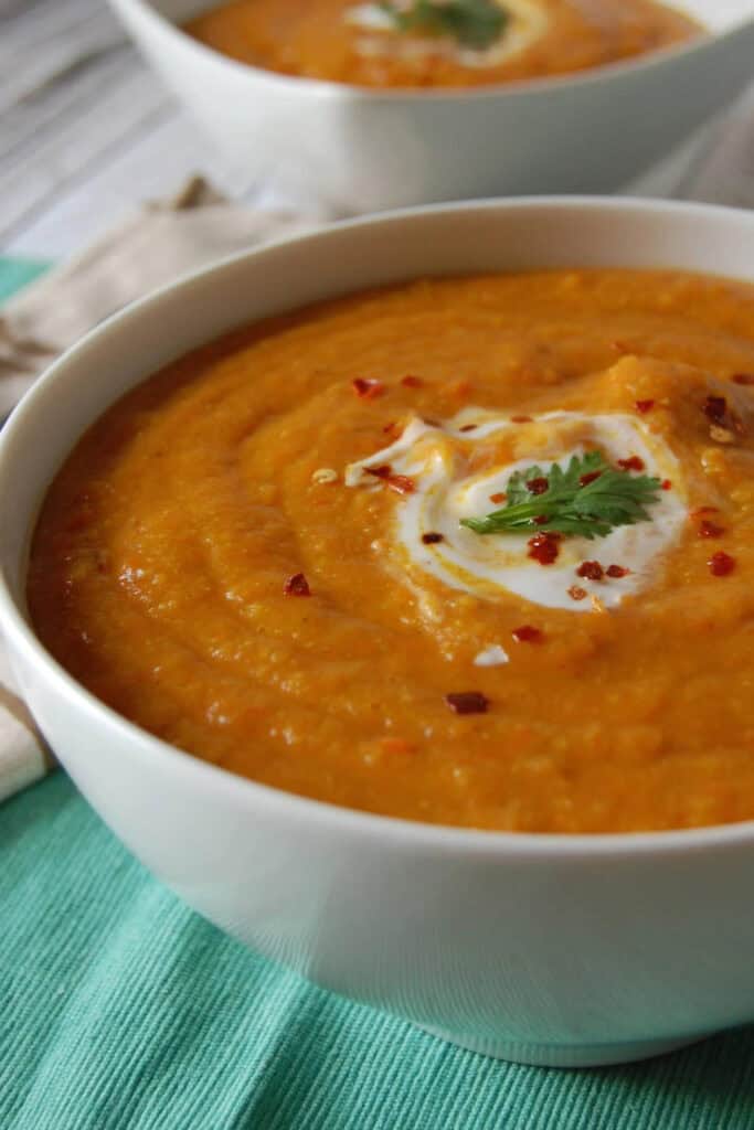 Two bowls of Morrocan Carrot Lentil Soup with a swirl of yogurt and parsley.