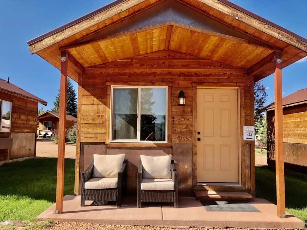 Cute, small wooden cabin with two chairs in front at Mountain Ridge Cabins & Lodging.