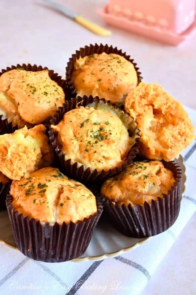Golden-brown mozzarella cheddar muffins stacked on a plate, with melted cheese peeking through and a sprinkle of herbs on top.