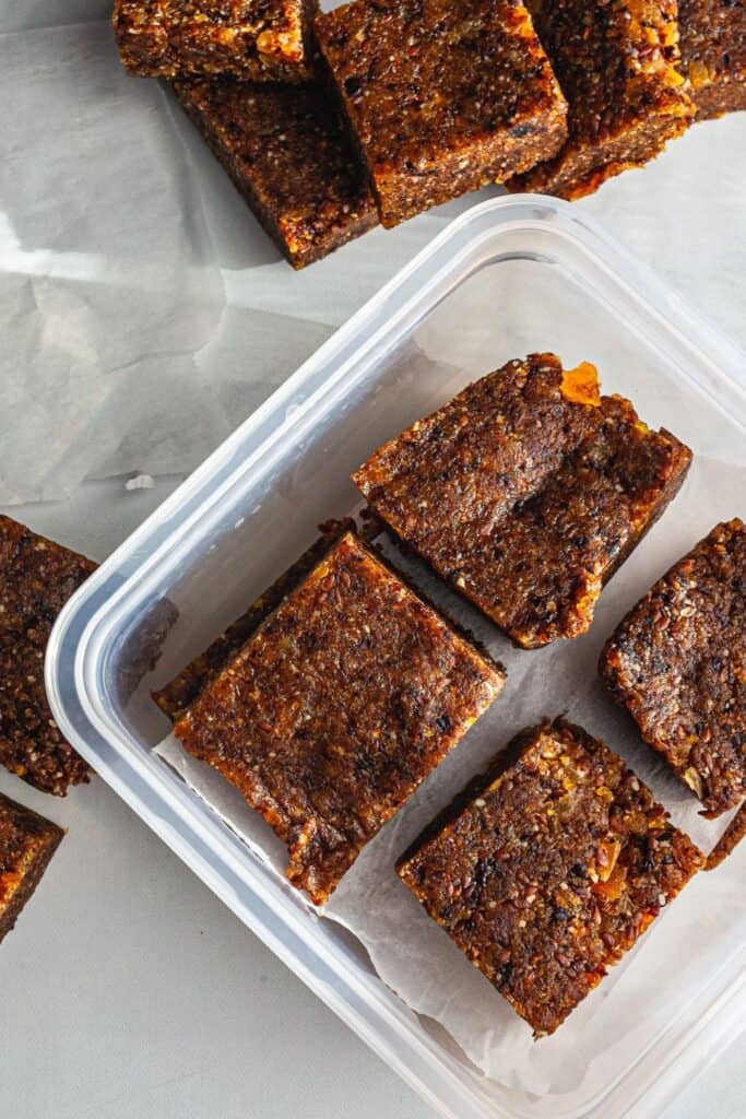 A plastic to-go container filled with walnut, almond, apricot squares. 