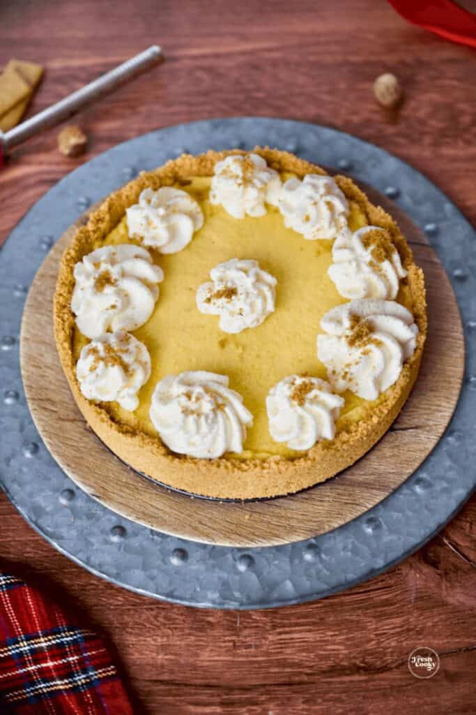 No bake eggnog pie in a golden graham cracker crust, topped with swirls of whipped cream and a sprinkle of nutmeg. Displayed on a rustic wooden table with holiday touches, making it a festive and easy Christmas dessert.