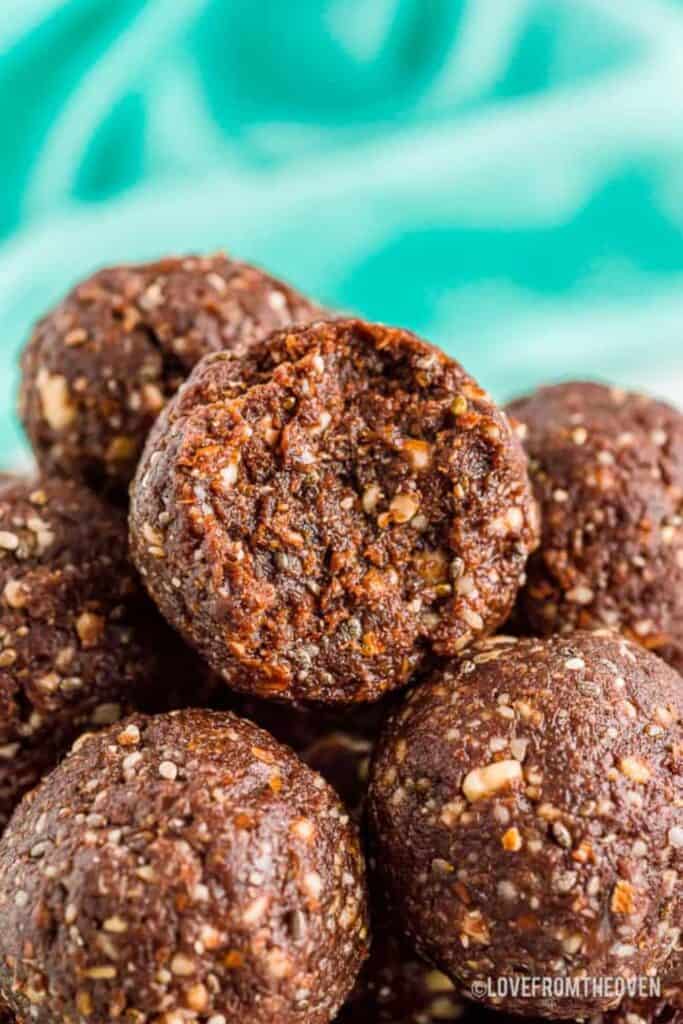 Close up of no bake energy bites stacked together, showing a rich chocolate brown color with visible oats, seeds, and small nut pieces throughout.