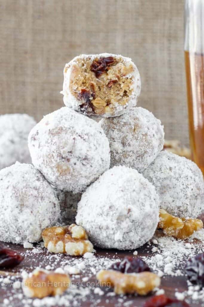No Bake Gingersnap Brandy Balls rolled in powdered sugar, stacked with one bite showing a chewy center filled with crushed cookies, dried fruit, and nuts.