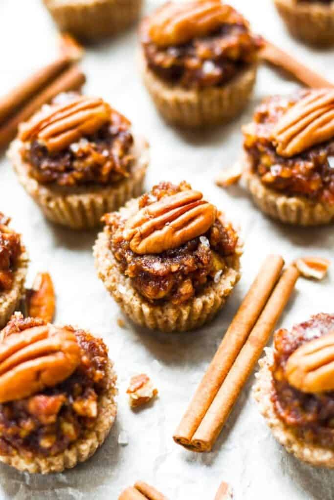 No Bake Pecan Pie Mini Tarts with a chewy, nutty filling topped with whole pecans, nestled in golden crusts and surrounded by cinnamon sticks.