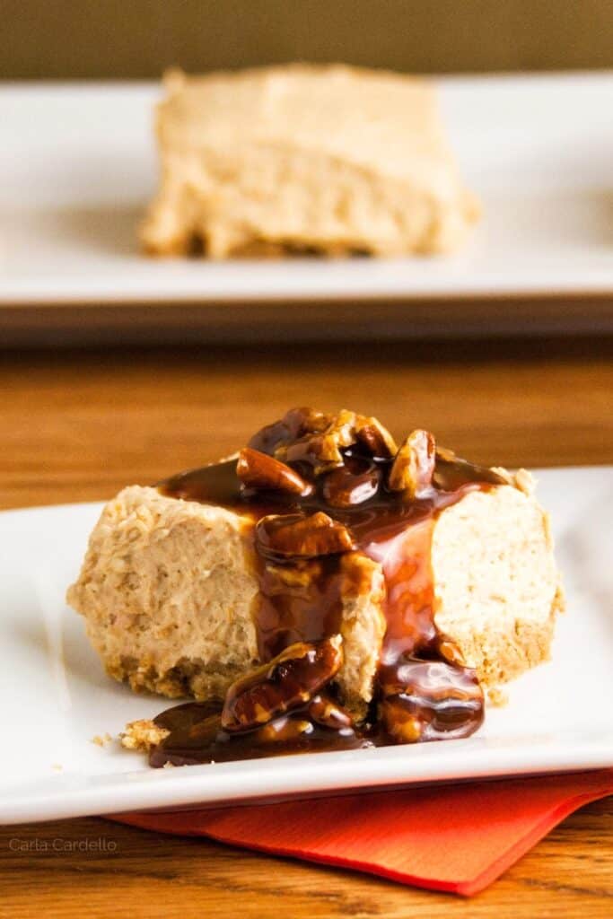 A single creamy pumpkin cheesecake bar sits on a white plate with caramel and pecans dripping down the sides on a plate.
