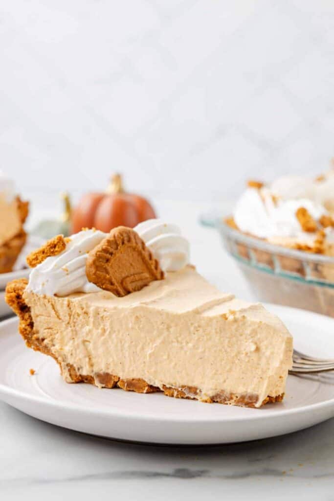Slice of no bake pumpkin pie with a thick creamy filling and spiced cookie crust. Whipped cream and a Biscoff cookie top the chilled fall dessert.